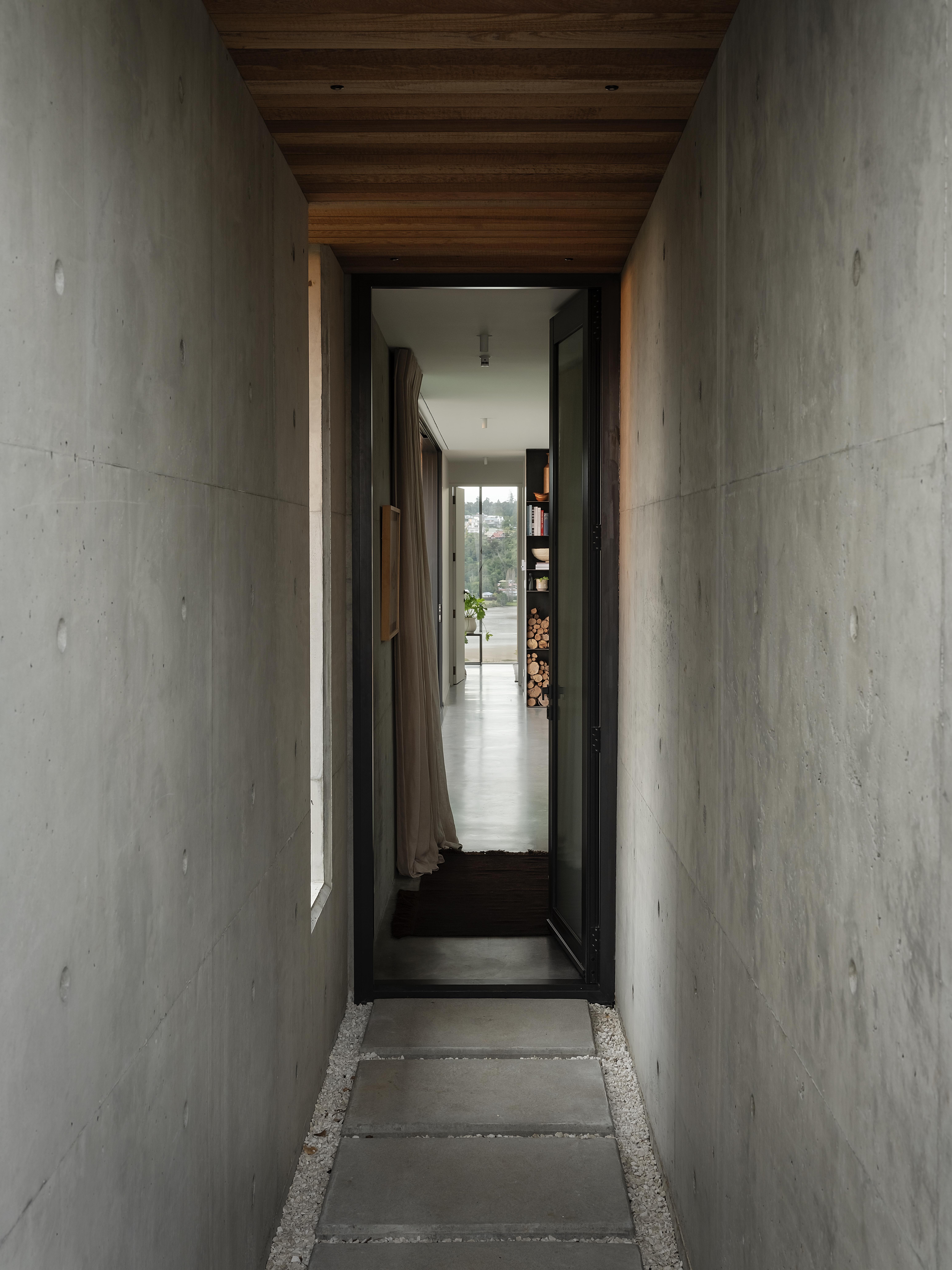 MDA House by Matt Deeb Architecture: Partially opened black-framed glass door leading to a room with a wooden bed frame, white bedding, and a gray cinder block wall.