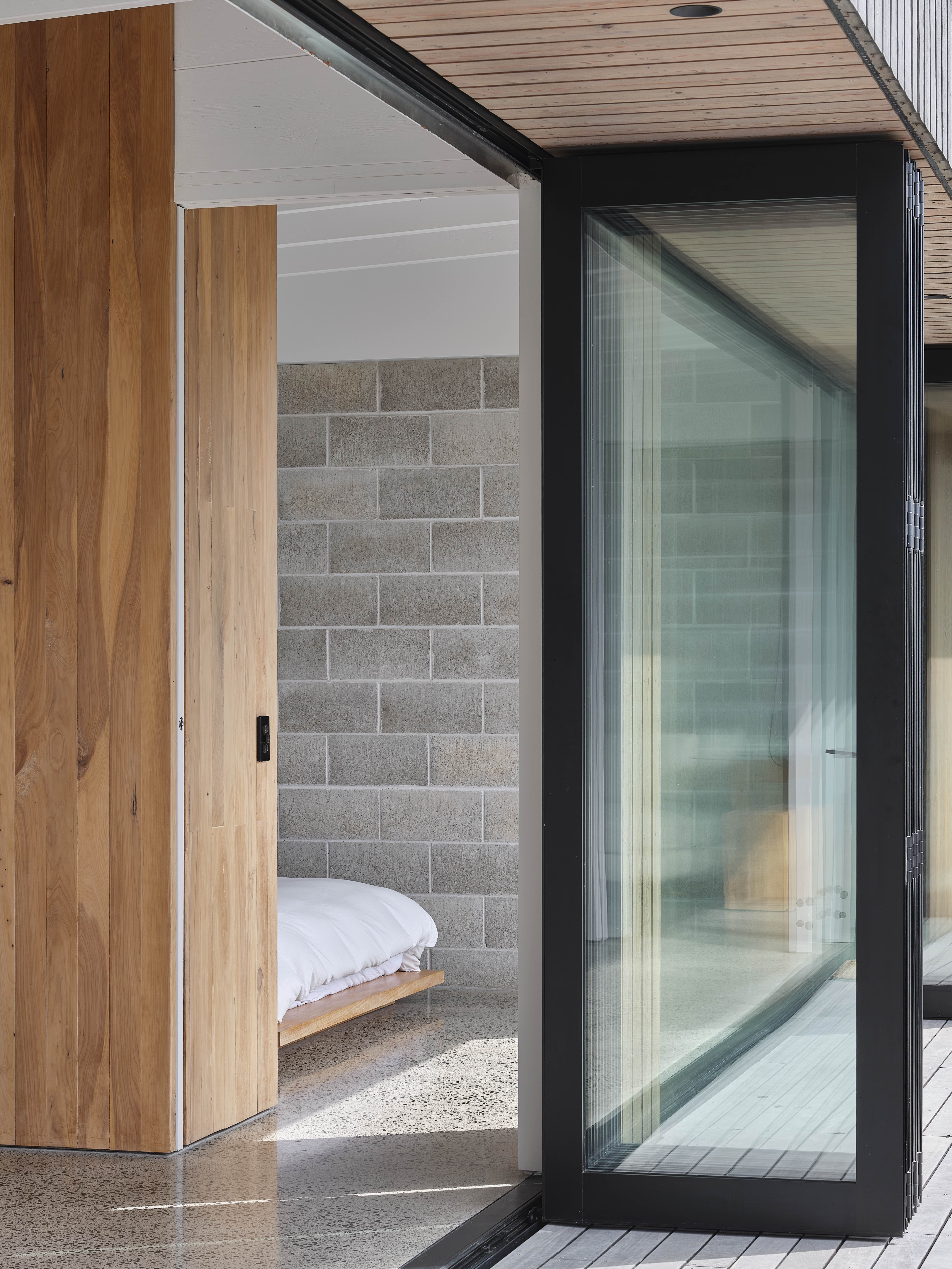 MDA House by Matt Deeb Architecture: Interior view of a modern room with a stone block wall, wooden sliding door, and a partially visible white bed.