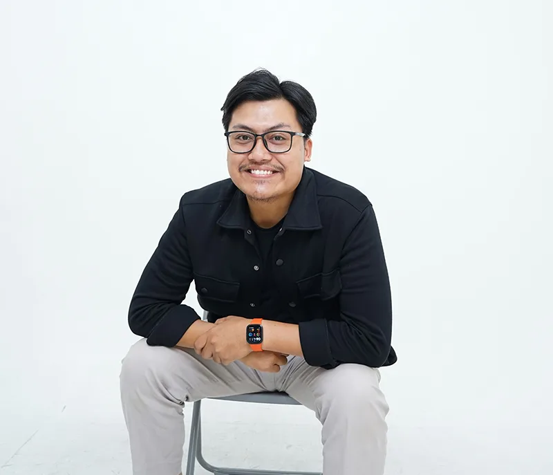 Portrait of a man sitting and smiling against gray background.