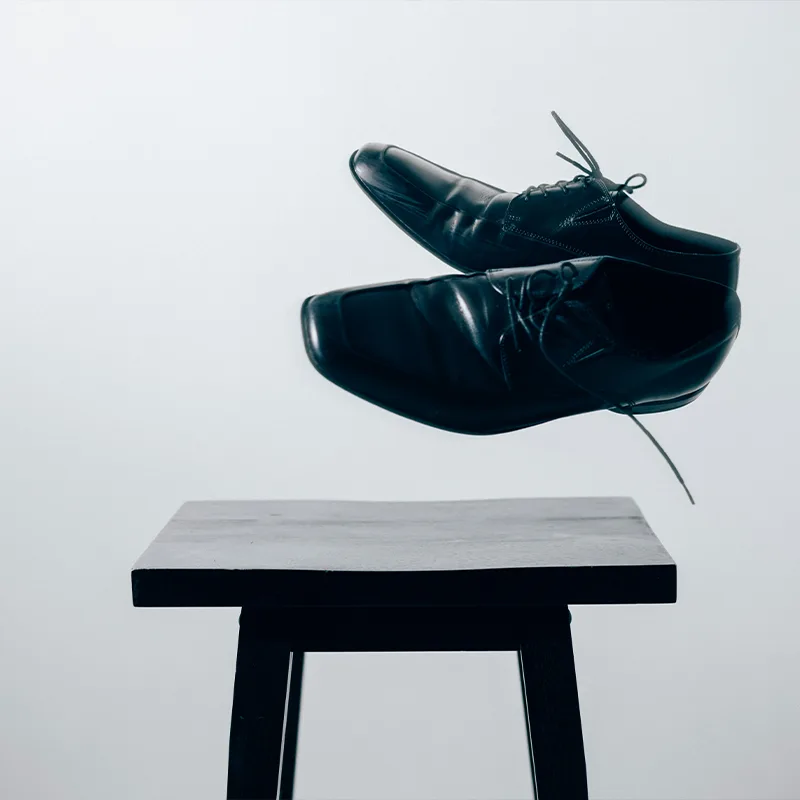 Black modern chair and flying shoes against white background.