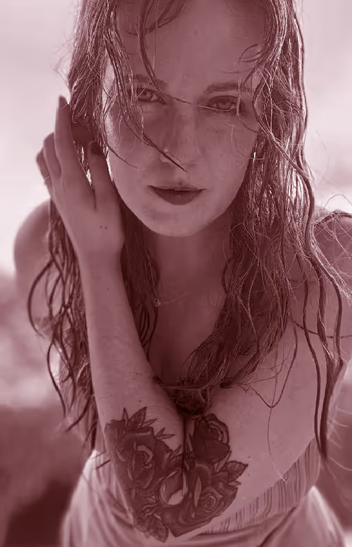 Natalie touching her face, showing a tattoo of roses on her forearm.