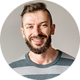 Smiling man with a beard and short hair wearing a striped shirt against a neutral background.
