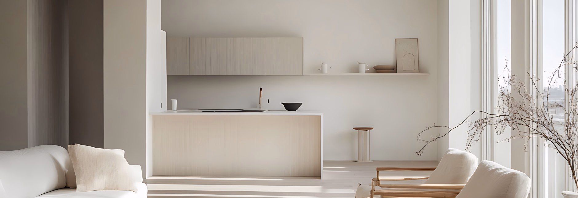 Minimalist open kitchen with light wood island, white cabinets, a stool, and neutral-toned seating near large windows with natural light.