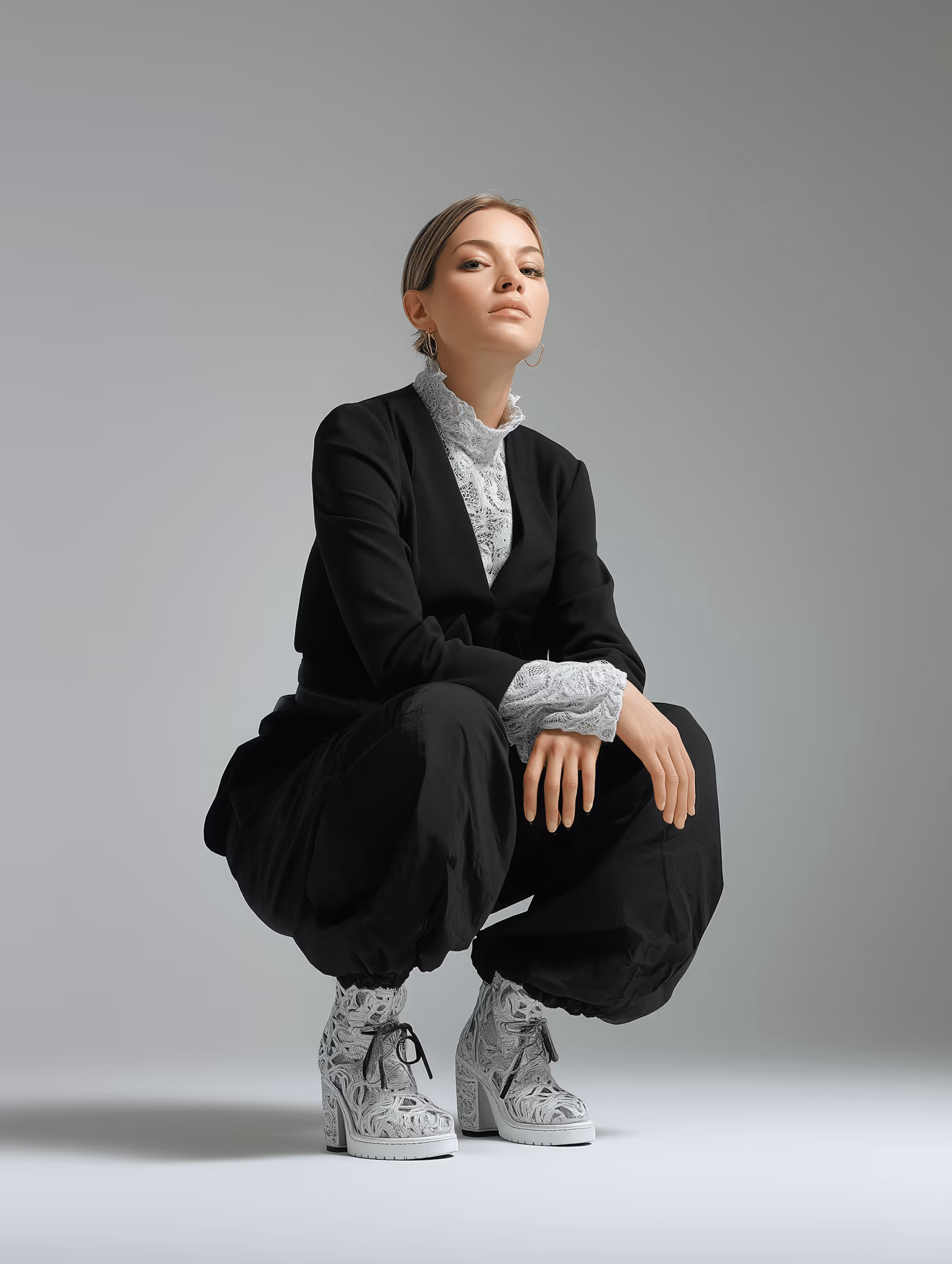 Woman in black outfit with lace cuffs and collar crouching, wearing white patterned lace-up heeled boots.