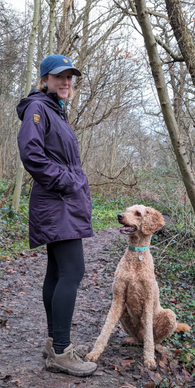 Rebecca from Trent Dog Walking standing in woodland with Omar, a curly-haired Poodle cross