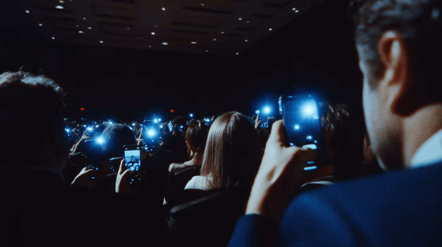 Groupe de personnes dans une salle sombre prenant des photos avec leurs téléphones allumés.