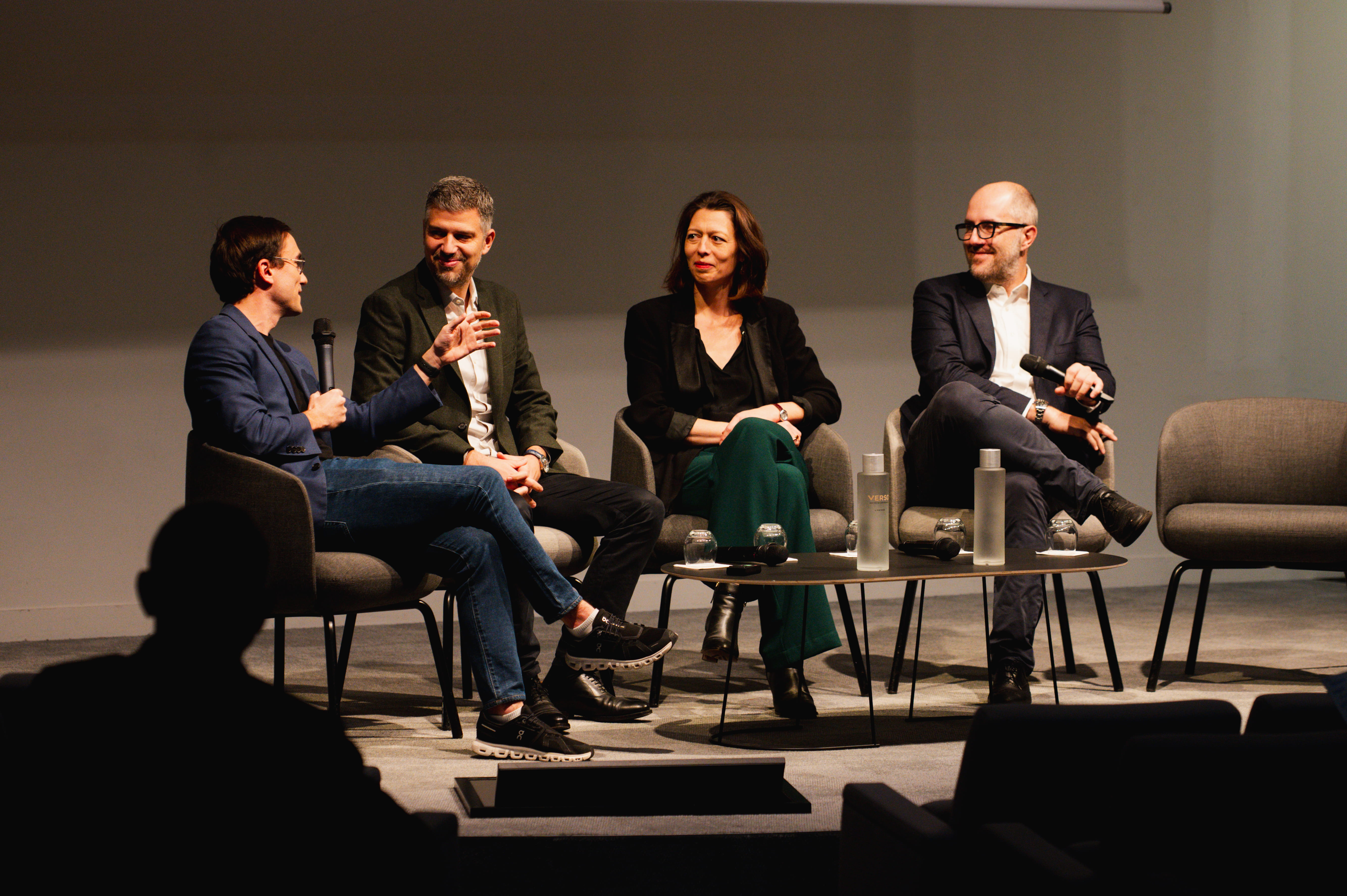 Quatre personnes assises sur des fauteuils sur une scène lors d'une table ronde, deux d'entre eux tenant un micro.