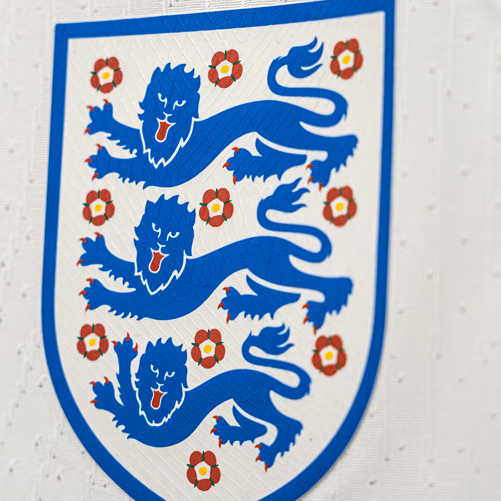 Close-up of England football team badge with three blue lions and red roses on white background.