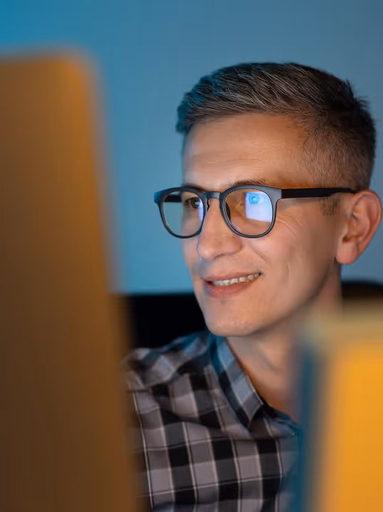 Smiling man wearing glasses working at a computer.