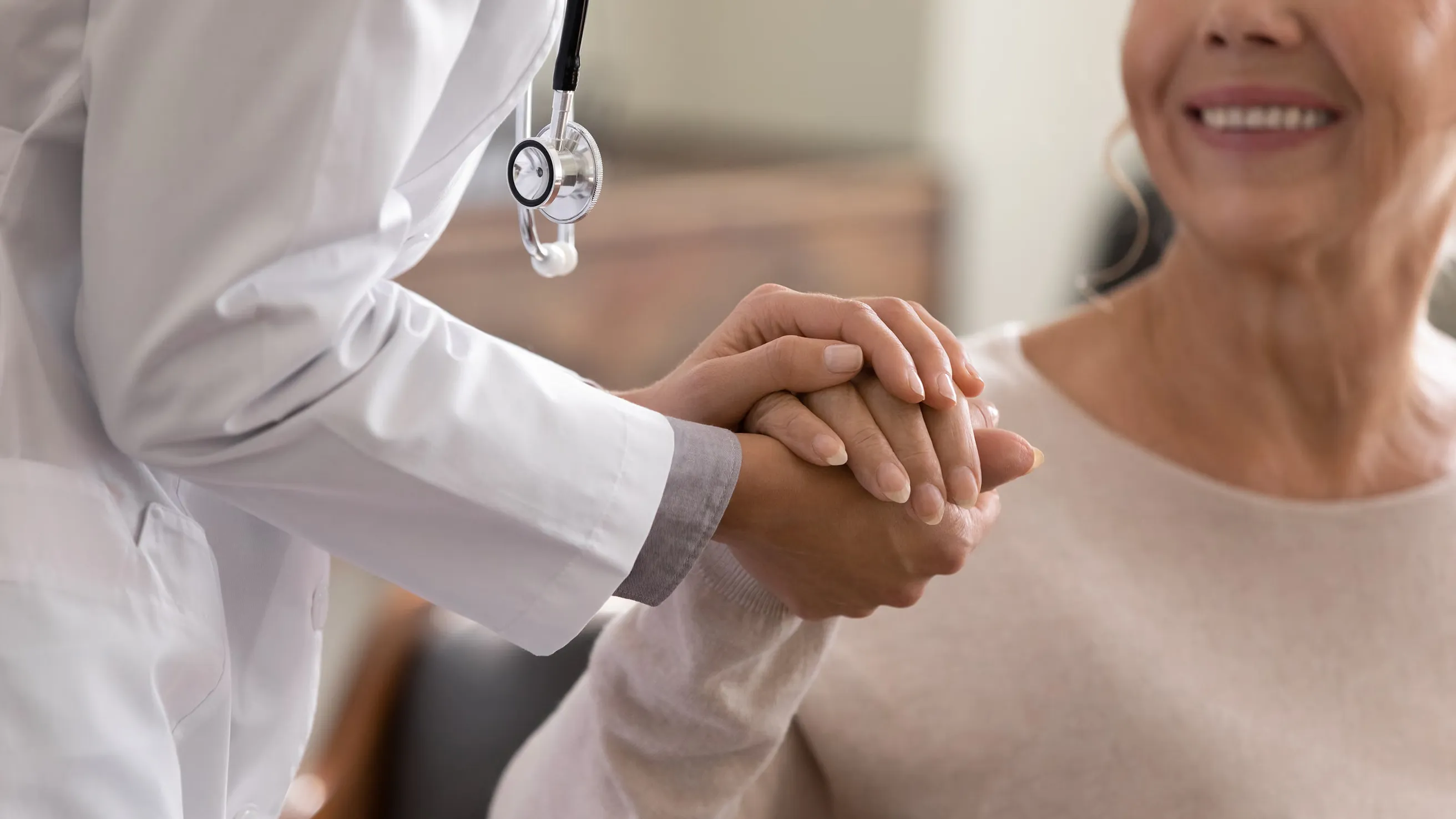Doctor holding patient’s hand in a reassuring gesture during a medical visit.
