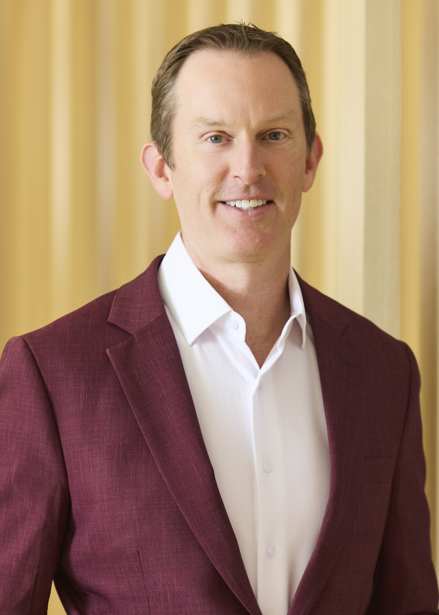 Professional headshot of smiling man in light purple shirt and dark tie.