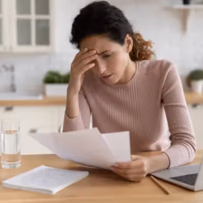 Patient sitting at a table holding papers with a concerned expression, a glass of water and a laptop nearby.