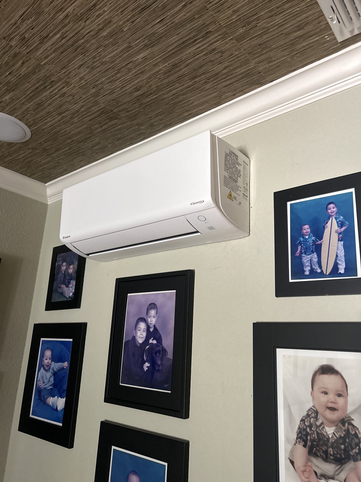 White Daikin indoor mini split air conditioning unit mounted on a wall above framed family photos of children.