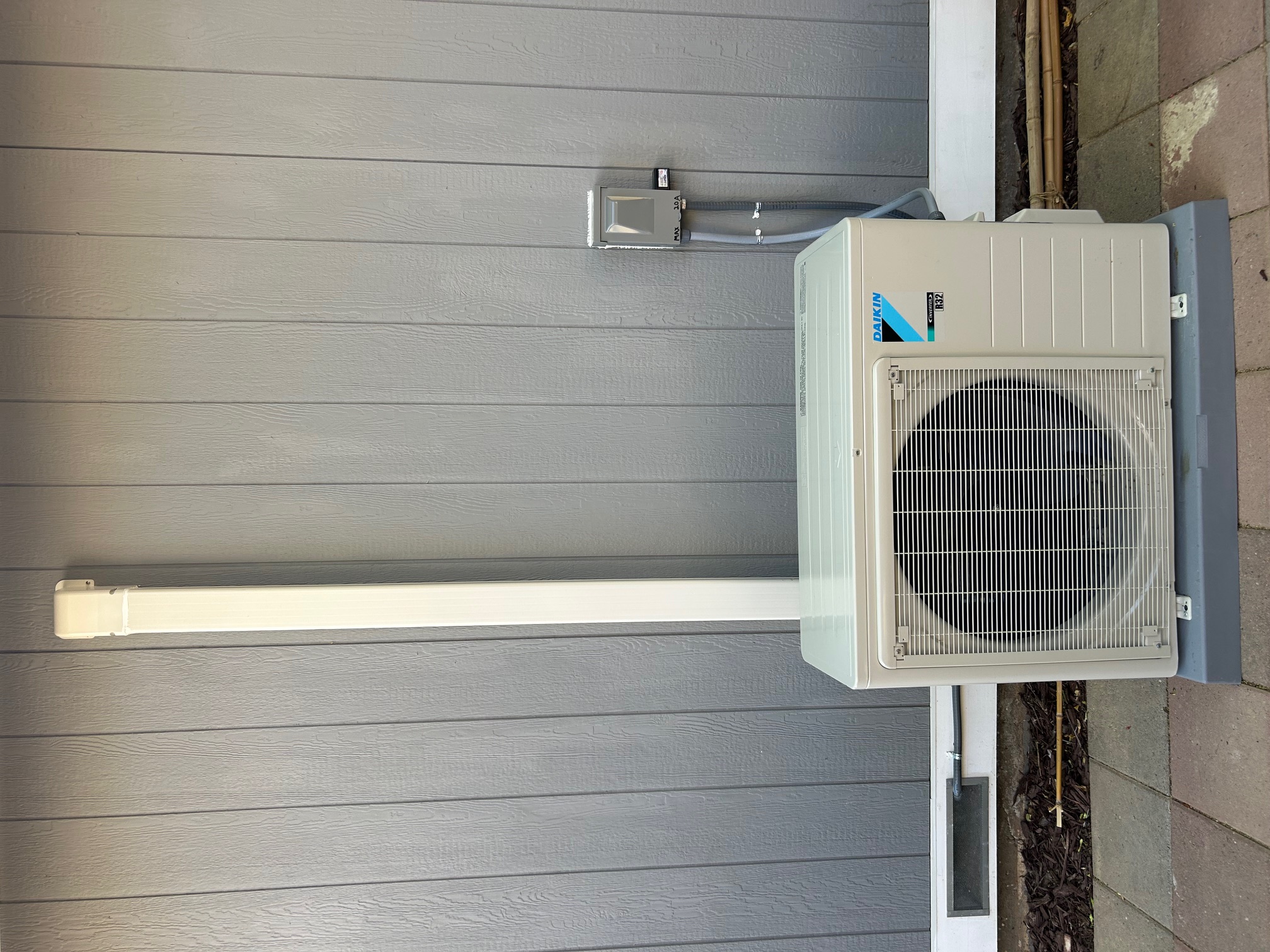 Daikin outdoor mini-split air conditioner condenser unit installed on a concrete pad against a gray paneled wall.