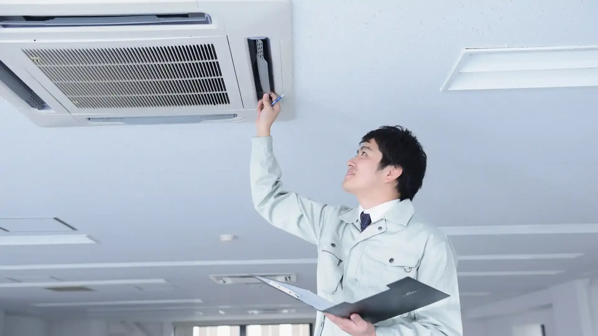 Technician inspecting a ceiling air conditioning unit while holding a pen and a folder.