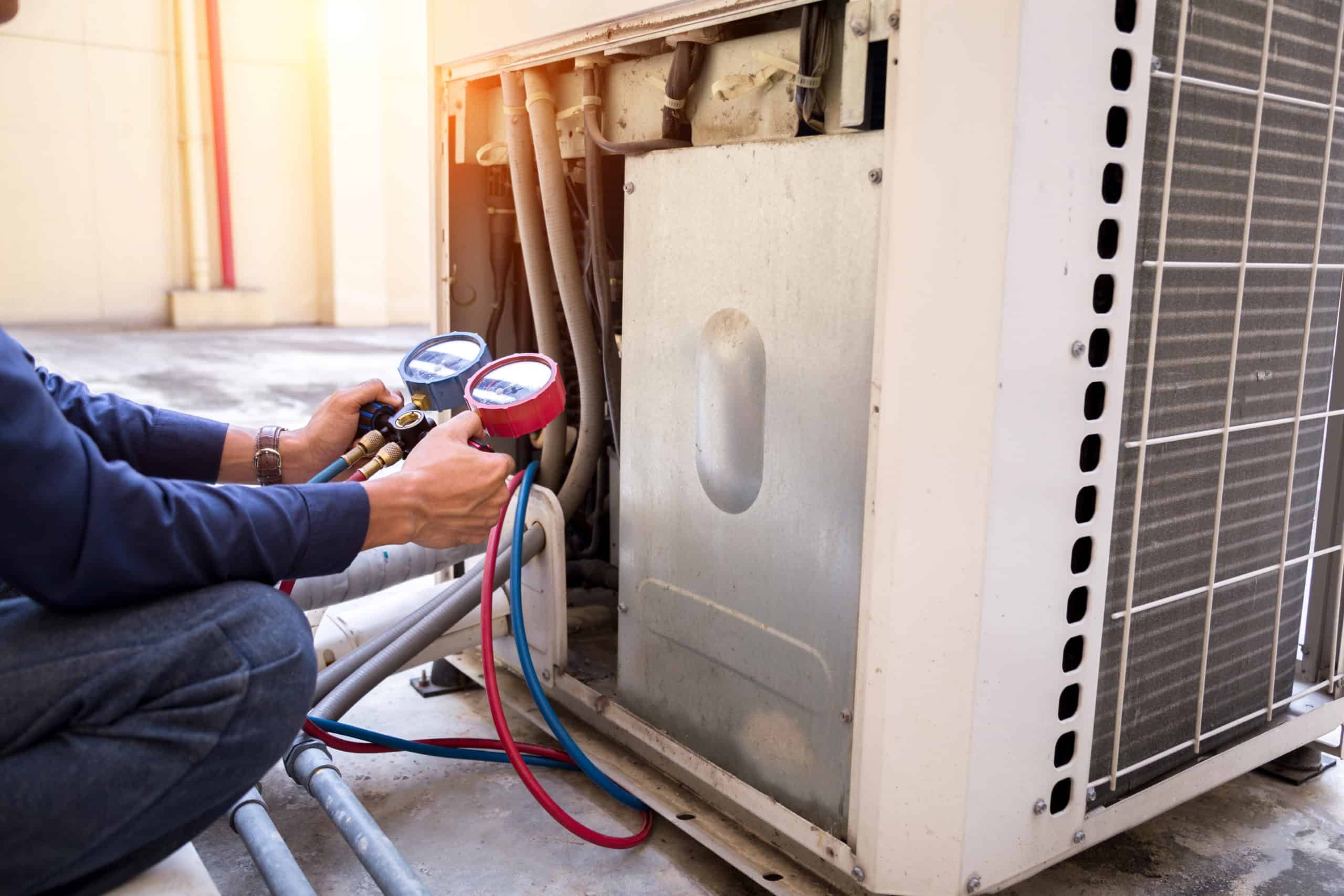 Technician using blue and red pressure gauges to check an outdoor air conditioning unit.