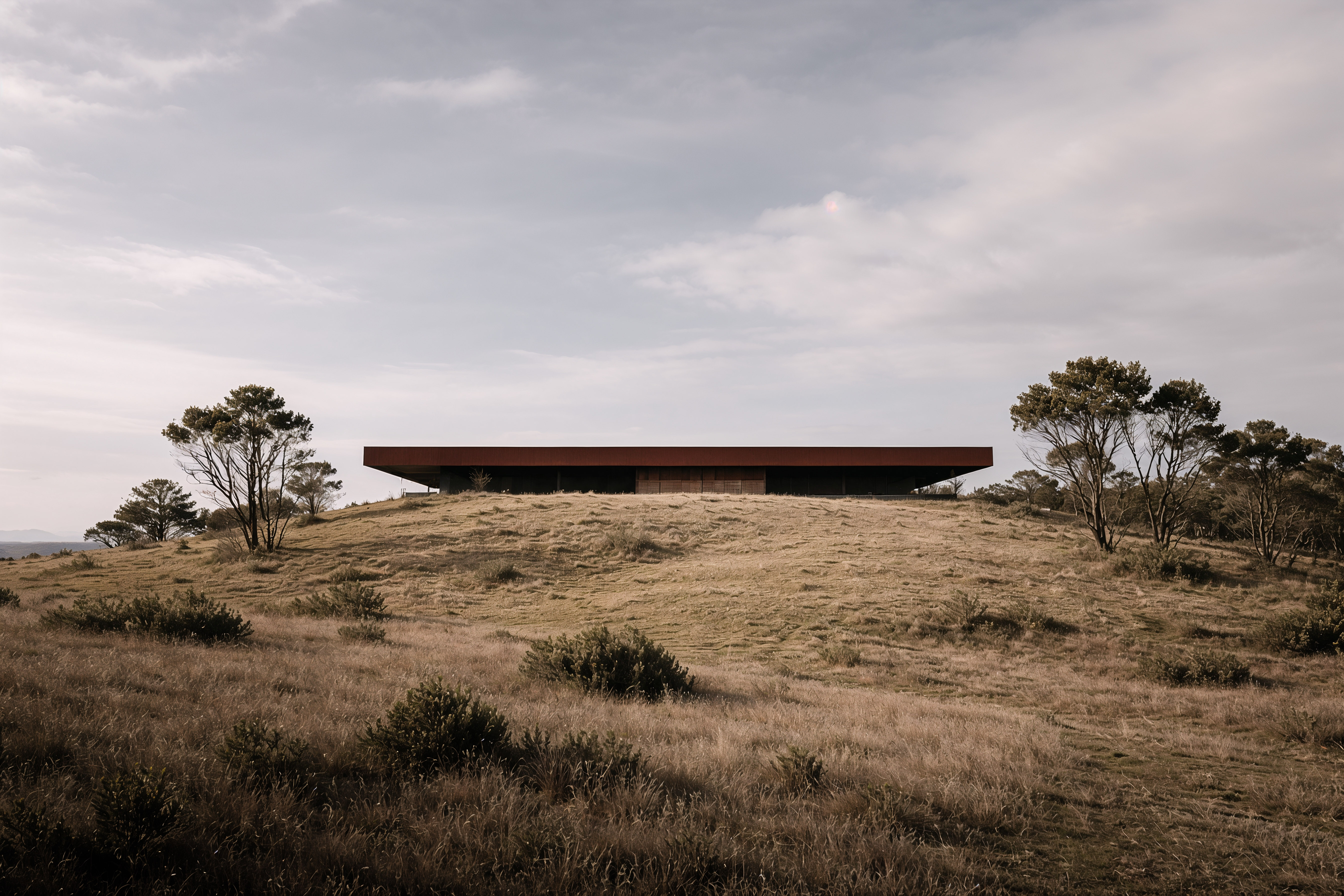Modern cantilevered stone and wood house in a mountainous landscape with two cars parked, one on a ramp and one beneath the overhanging section.