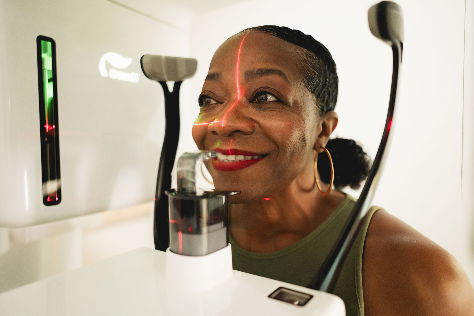 Woman with hoop earrings smiling as she undergoes a facial scan with red laser lines on her face.