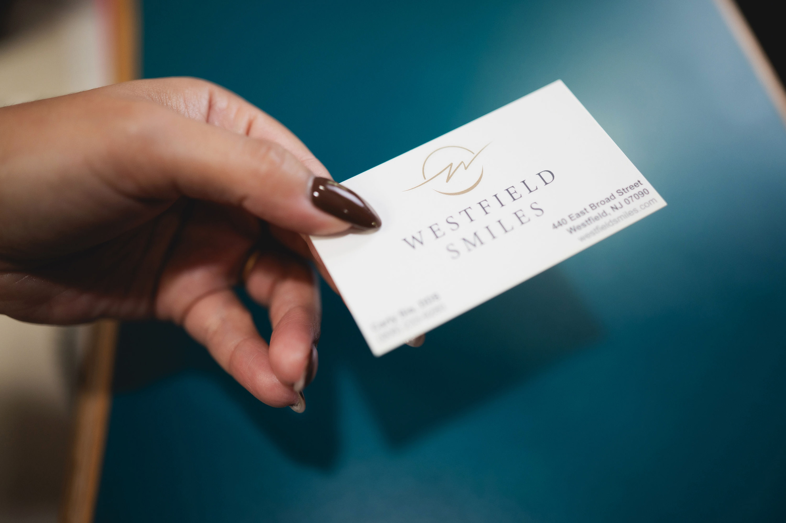 Hand with dark brown nail polish holding a Westfield Smiles business card.