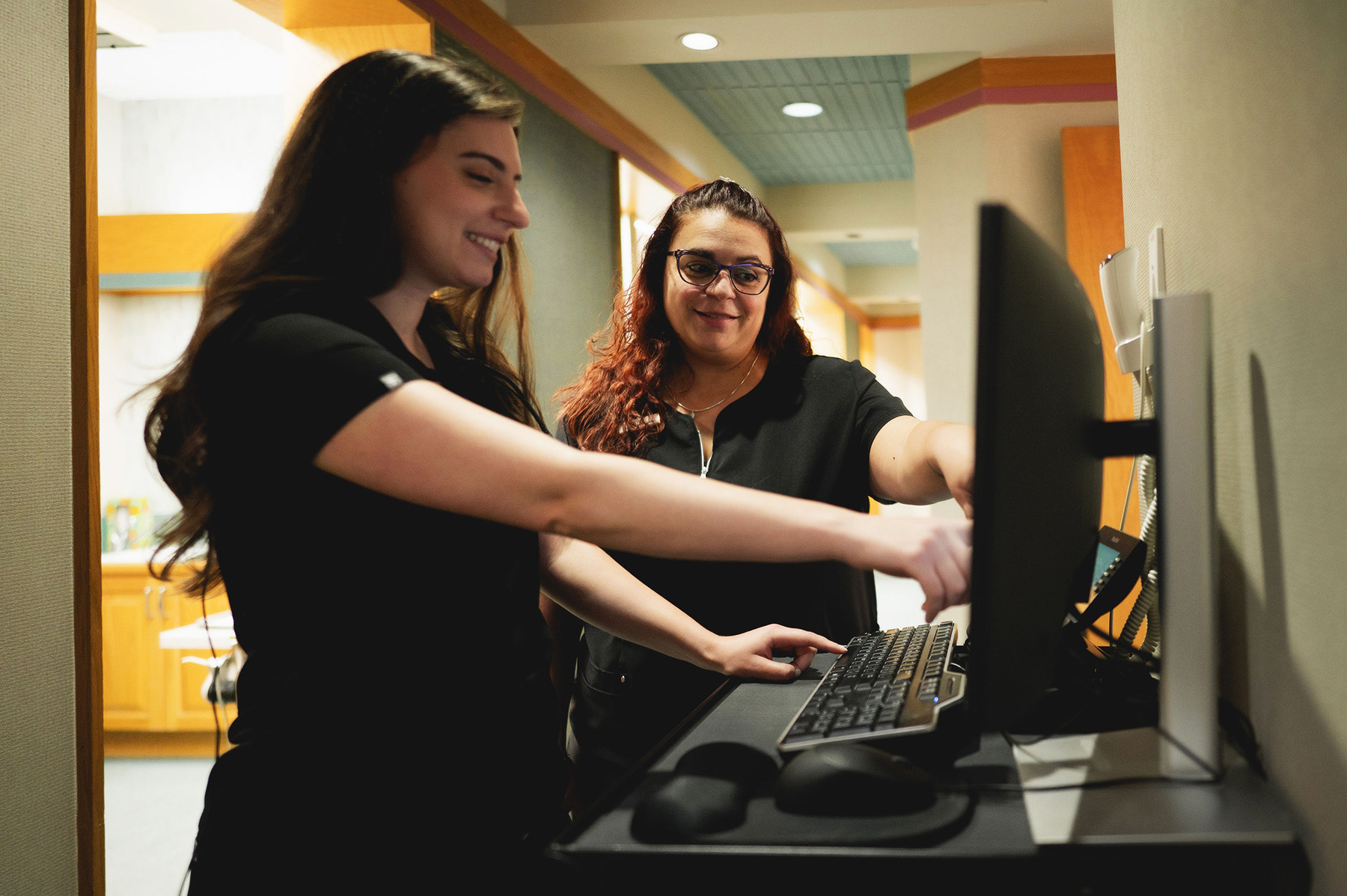 Two women in black uniforms interacting and pointing at a computer screen in a professional setting.