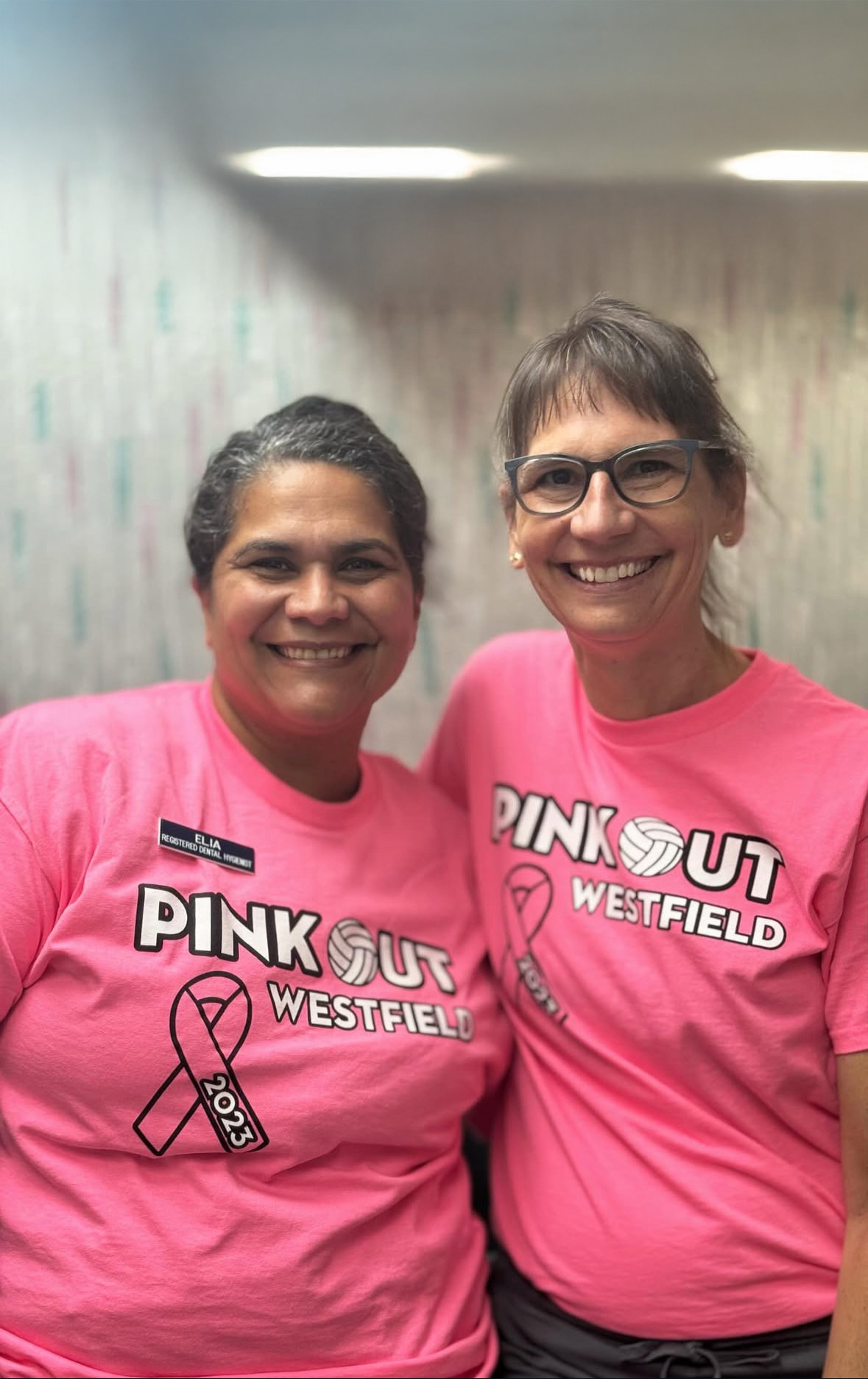 Two smiling women wearing matching pink 'Pink Out Westfield 2023' t-shirts, with one woman wearing glasses.