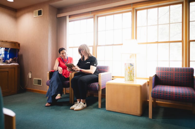 Two patients in a modern waiting room with large windows, seated on furniture in a clinical setting