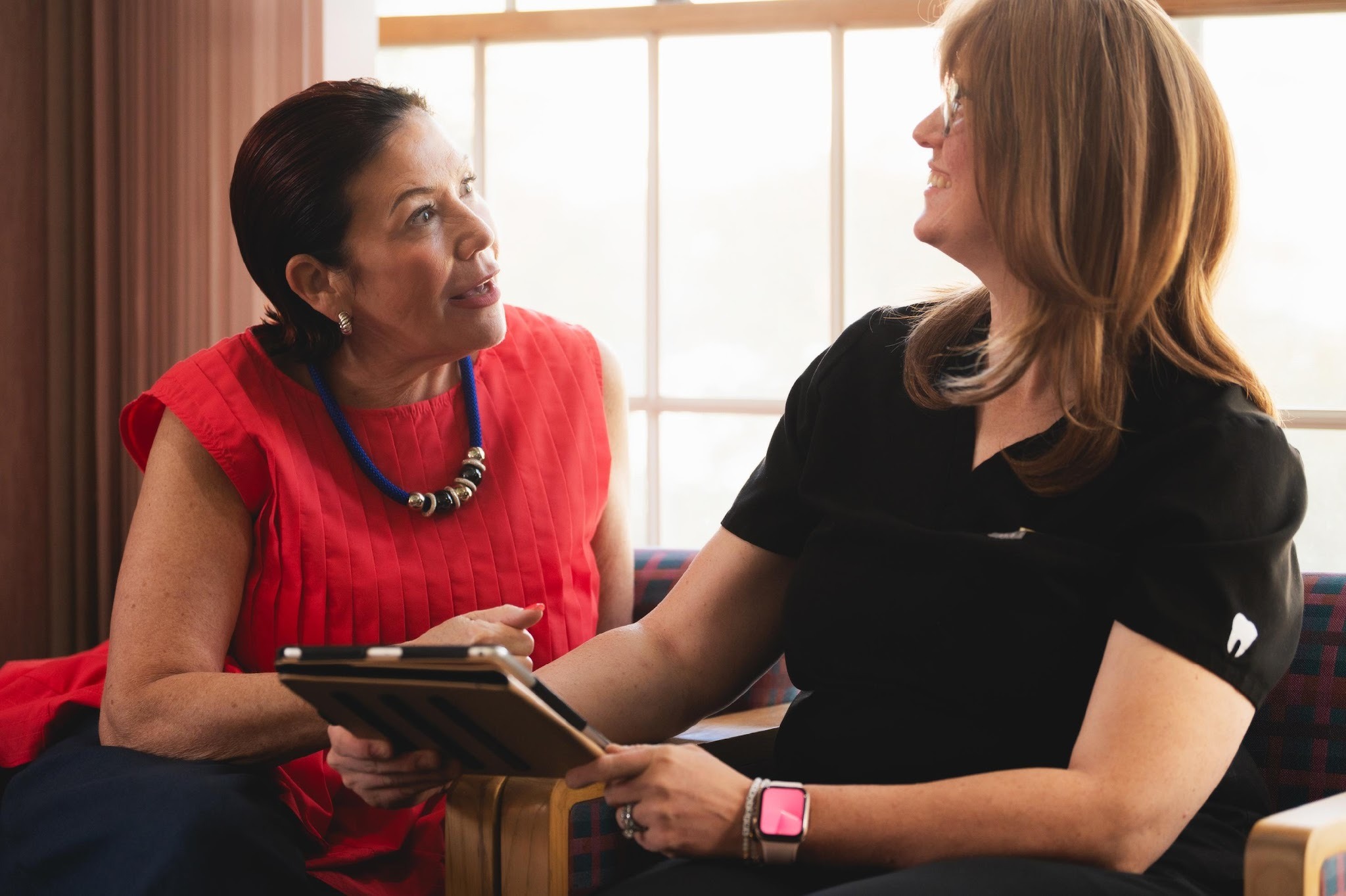 Two dental professionals consulting with patient in warm, well-lit office environment
