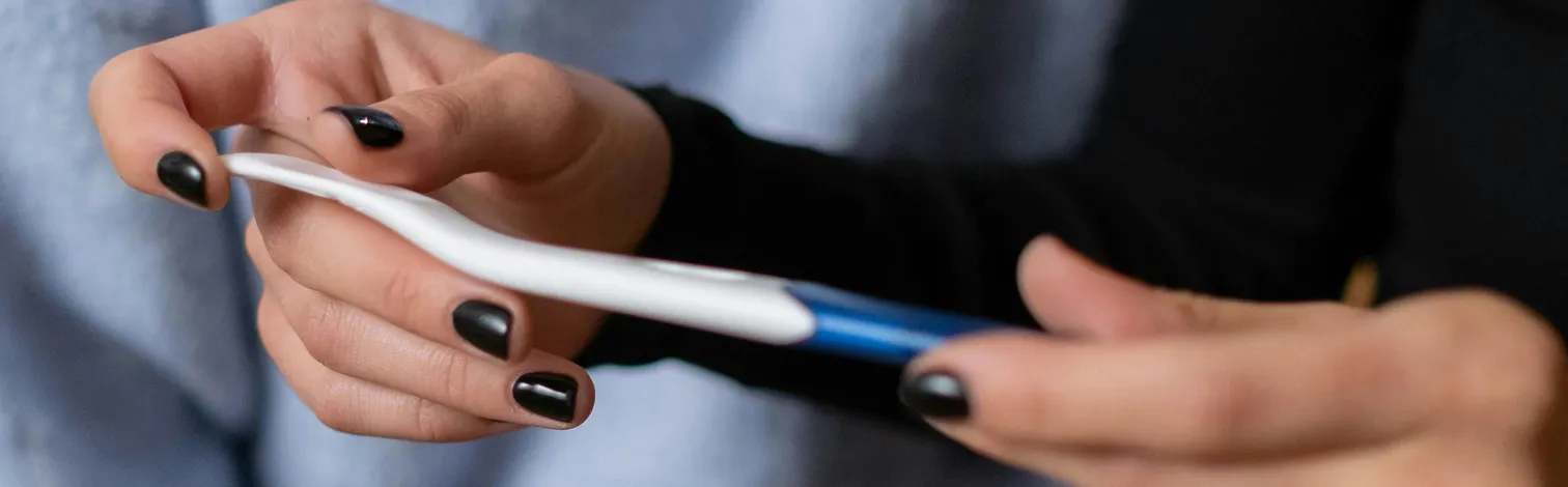 Person with black nail polish holding a pregnancy test.