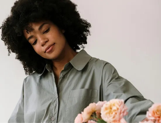 Young woman with curly hair wearing a green shirt arranging pink flowers.