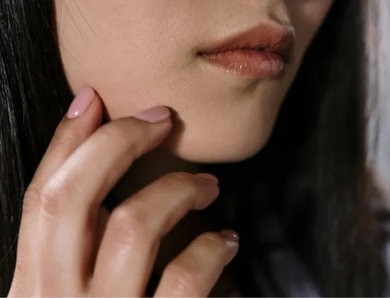Close-up of a woman's lower face with natural lips and a hand gently touching her cheek.