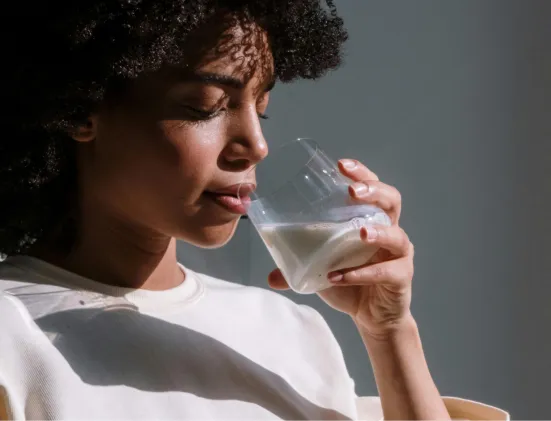 Close-up of a woman with curly hair drinking a glass of milk in soft natural light.