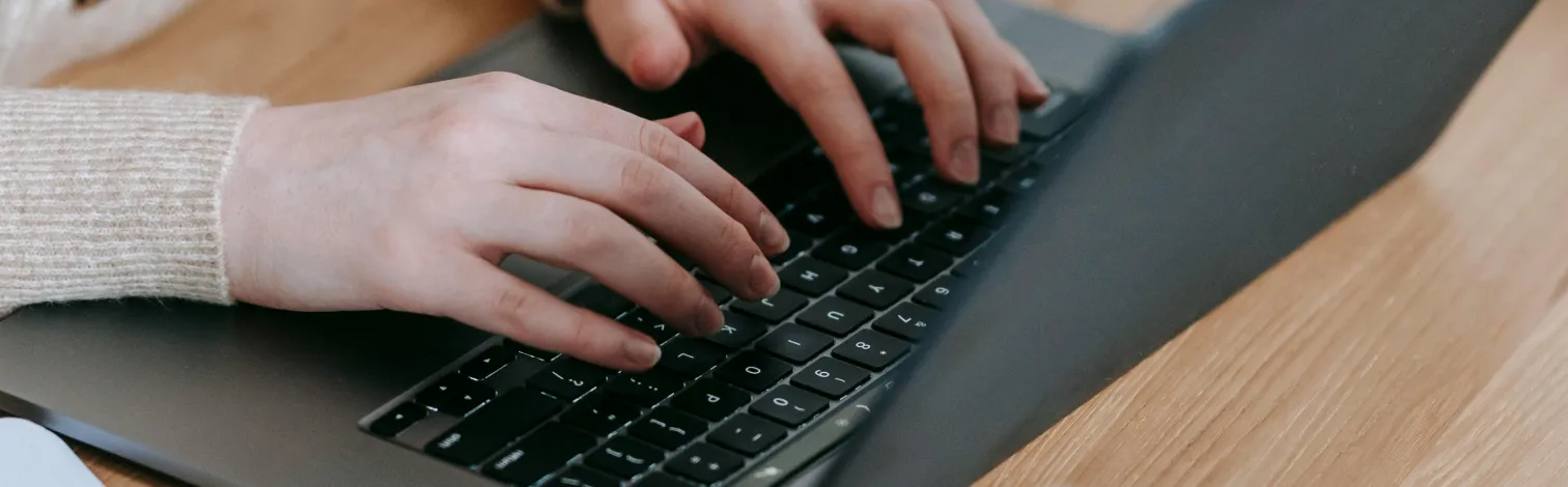 Person typing on a black laptop keyboard on a wooden desk.