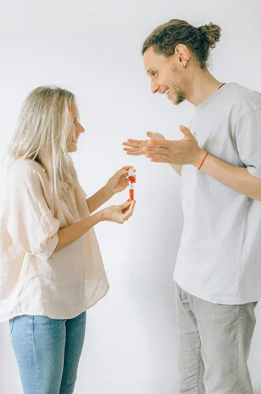 Smiling woman handing a small red gift to a happy man against a plain white background.