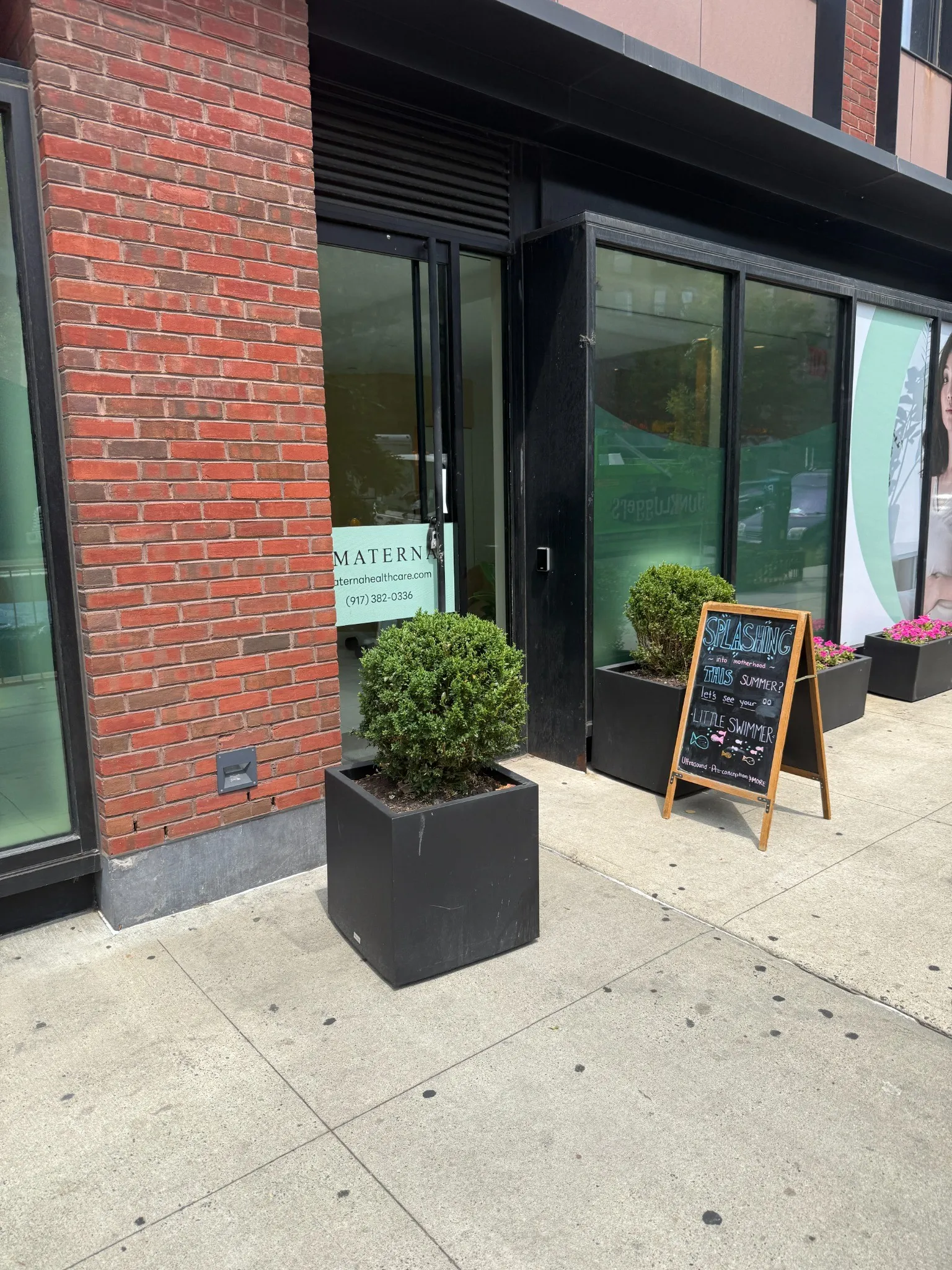 Materna storefront entrance with boxwood planters, a chalkboard sign and the practice sign in the window