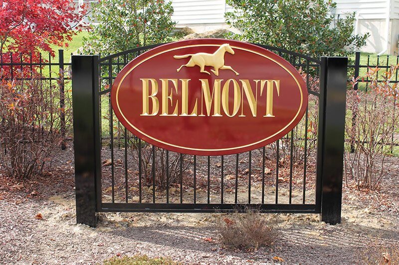 An oval carved sign mounted on an outdoor fence. The sign is painted red and has routed letters and border, painted gold. Above the text is a prismatic horse icon in gold.