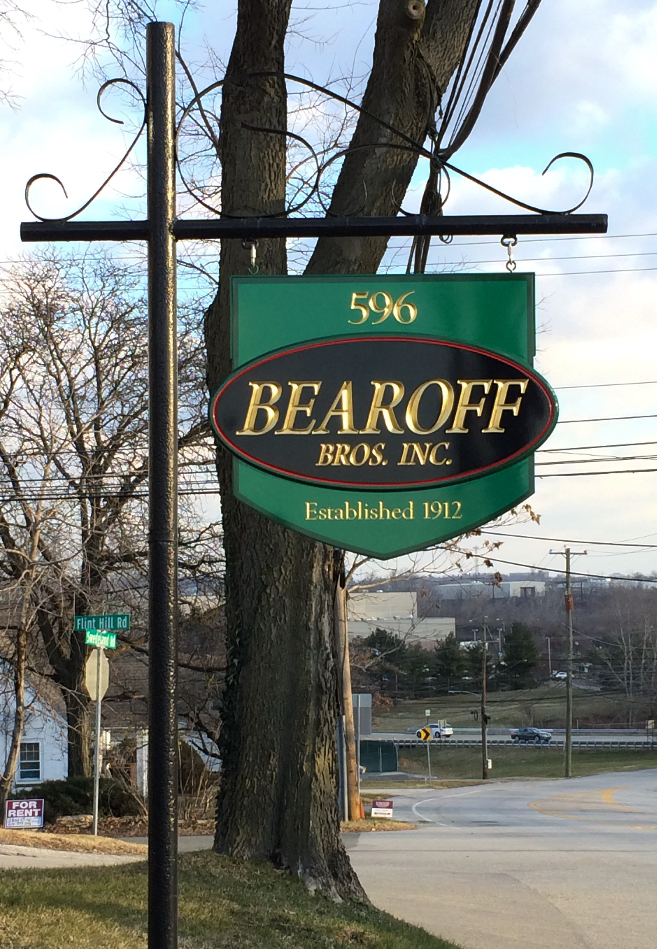 Gold lettering on a green and black carved HDU sign suspended from a scroll bar