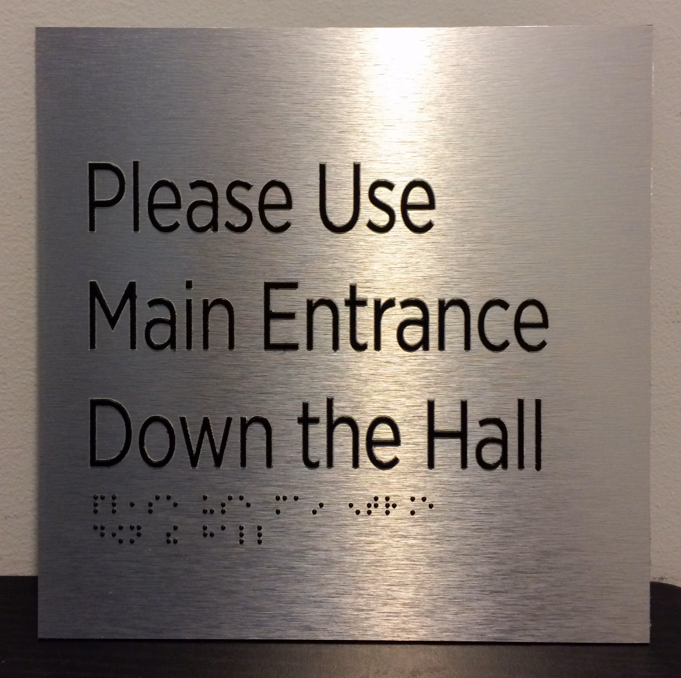 Black text and braille on brushed aluminum ADA sign