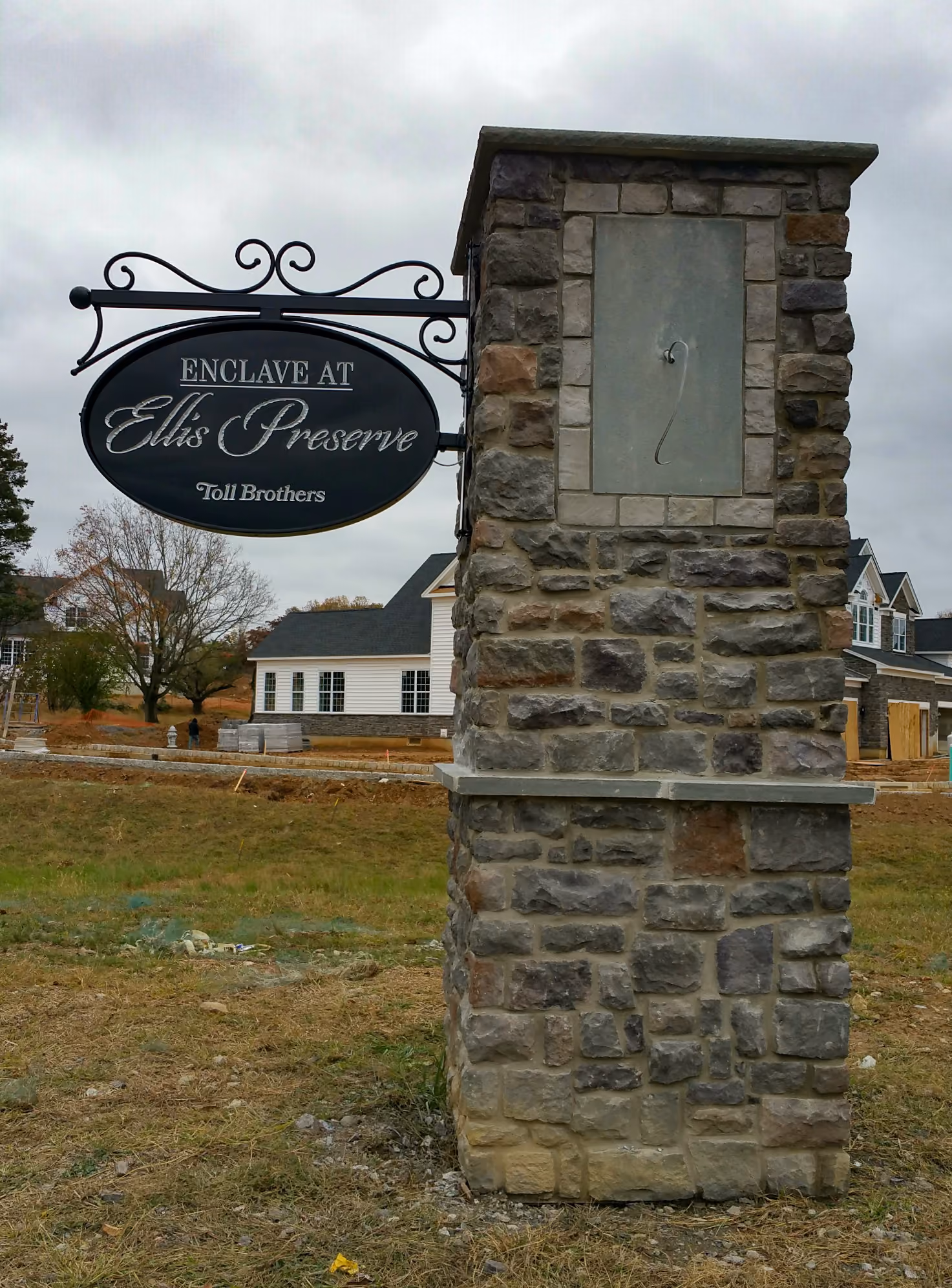 Oval carved HDU sign suspended from a scroll bracket on a stone pillar