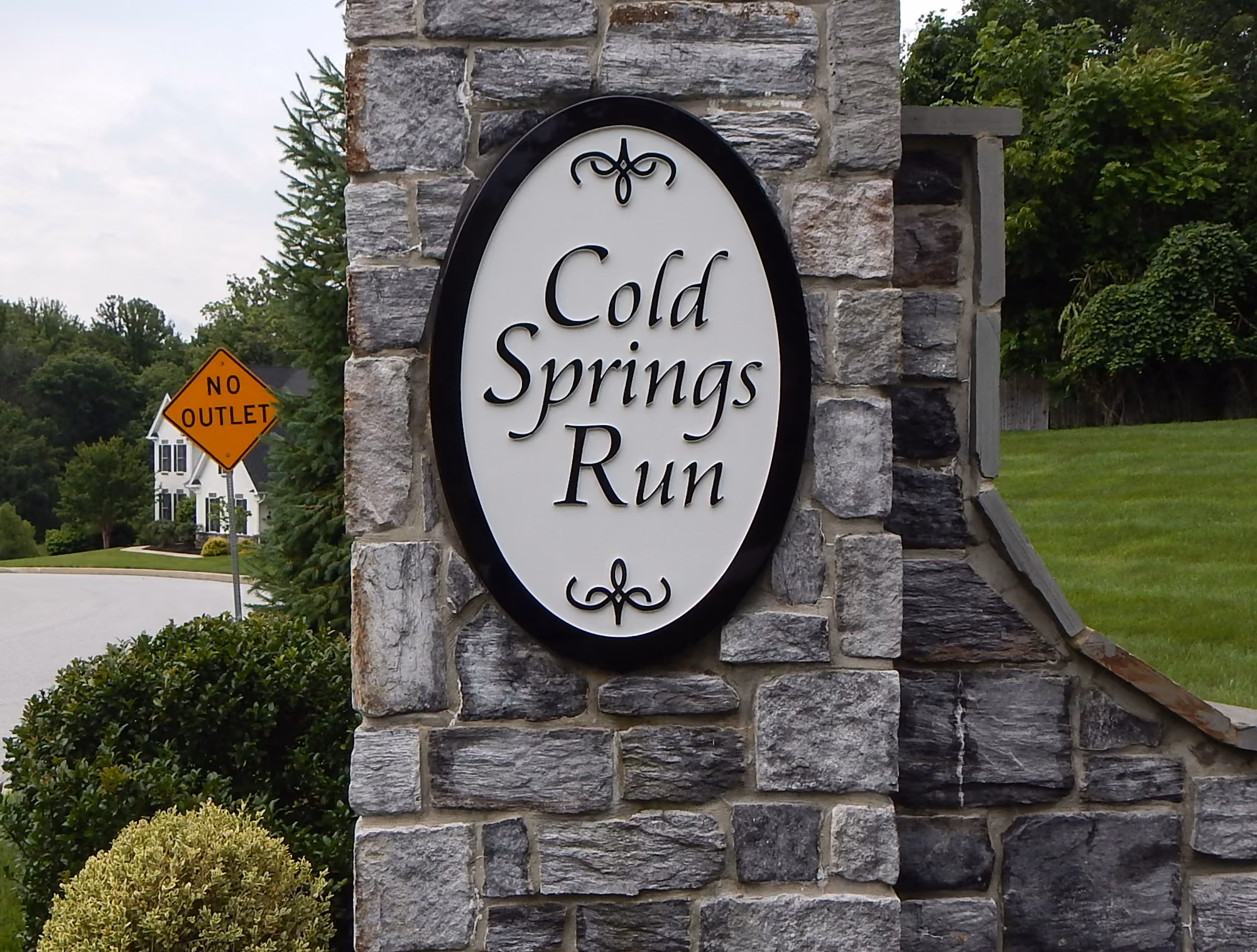 Tall oval carved HDU sign mounted on a narrow stone pillar