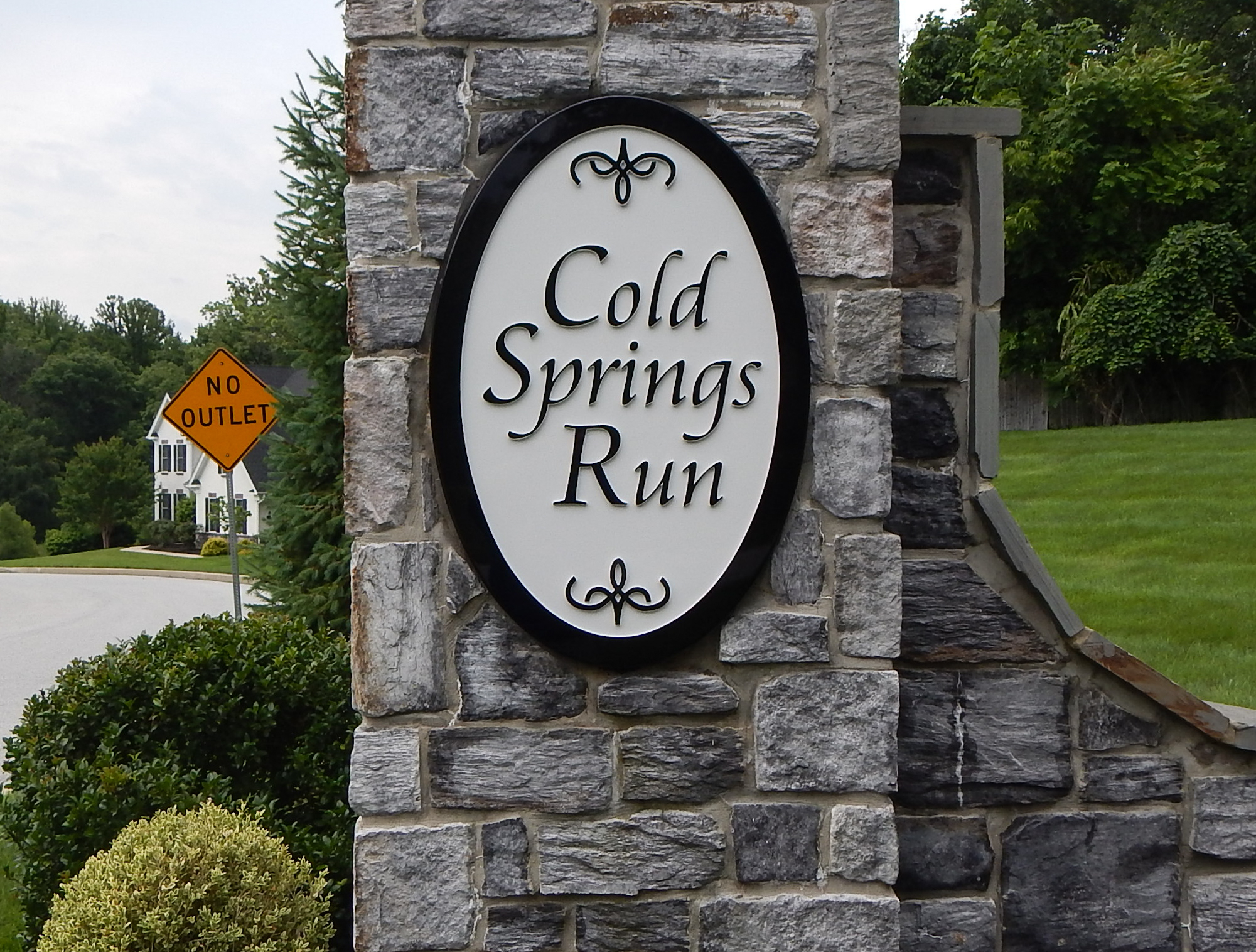 Tall oval carved HDU sign mounted on a narrow stone pillar