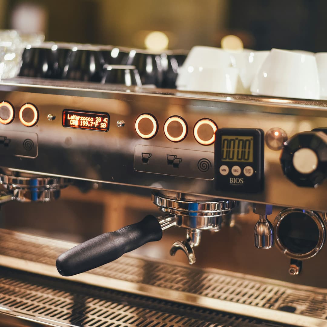 Detail profesionálního espressa s podsvícenými tlačítky, digitálním časovačem a šálky na vrchu.