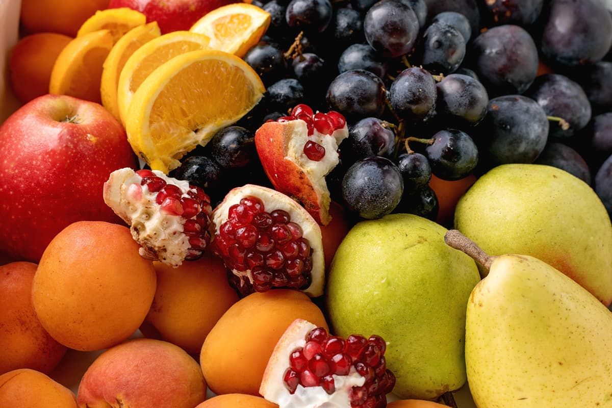Detailní záběr na různé druhy čerstvého ovoce, včetně nakrájených pomerančů, hroznů, jablek, hrušek, meruněk a semínek granátového jablka.