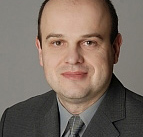 Portrét muže v šedém obleku a kravatě na neutrálním šedém pozadí.