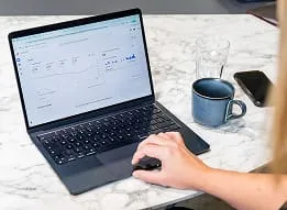 Person analyzing website traffic on laptop at marble table with coffee mug and smartphone.