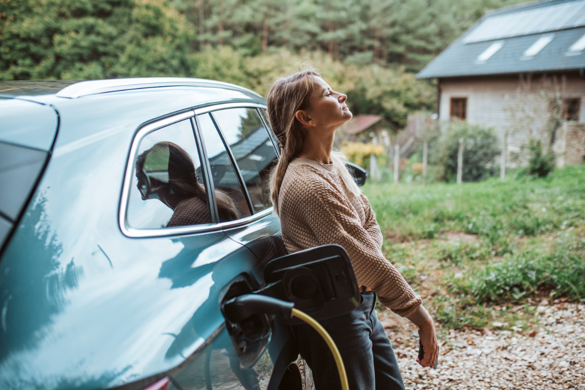 Frau lehnt an einem blauen Elektroauto, das geladen wird.