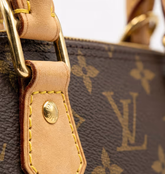 Gros plan sur une partie d'un sac à main Louis Vuitton en cuir marron avec logo LV et détails en cuir beige et métal doré.