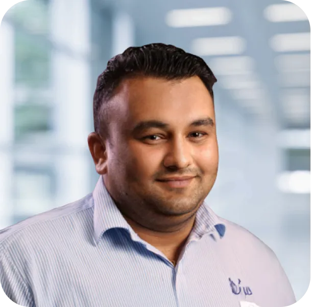 Smiling man with short dark hair wearing a light blue striped shirt in a brightly lit office setting.