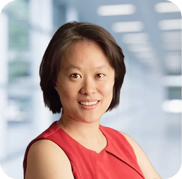 Smiling woman with short dark hair wearing a sleeveless red top, standing in a bright modern office background.