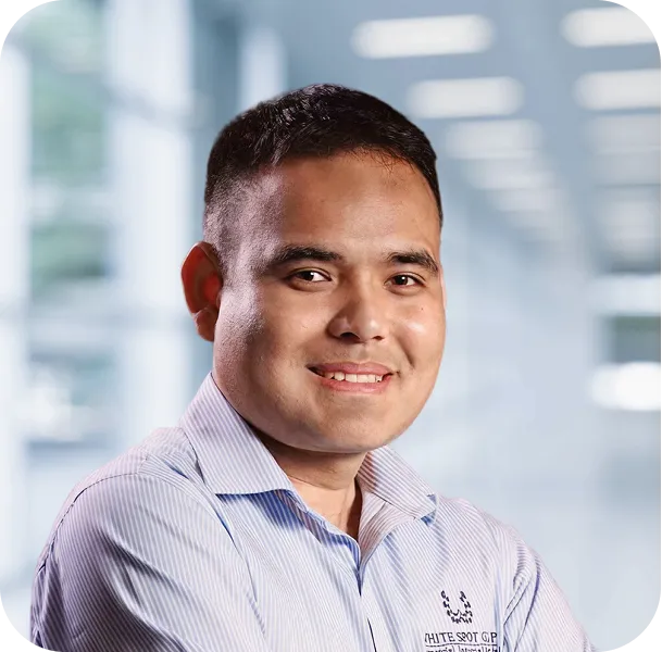 Smiling man wearing a light blue striped shirt with crossed arms in an indoor office setting.