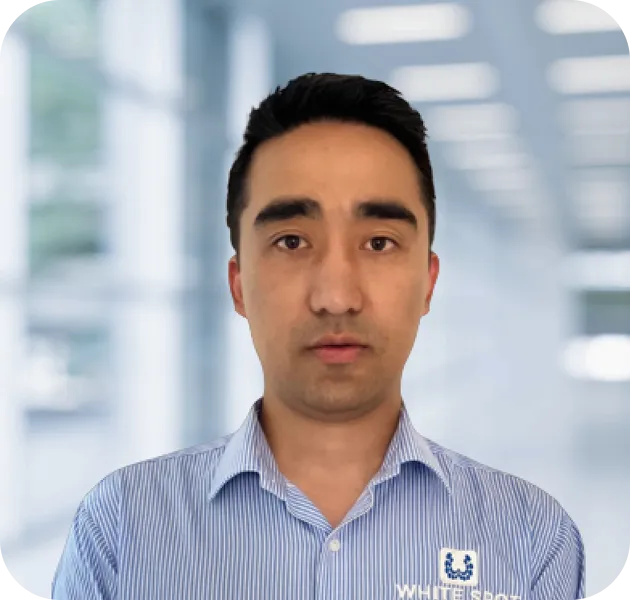 Portrait of a man with short black hair wearing a blue striped shirt in a modern office setting.